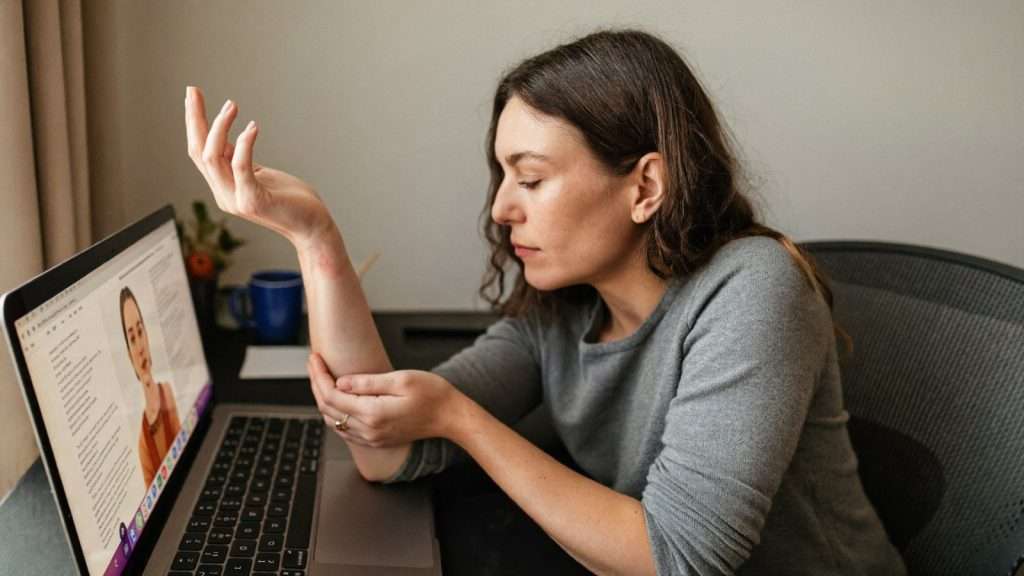 Frau am Schreibtisch hält ihr schmerzendes Handgelenk wegen Karpaltunnelsyndrom