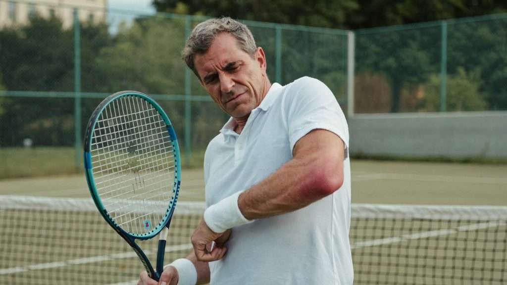 Mann mit Tennisarm greift sich auf dem Tennisplatz an den schmerzenden Ellenbogen